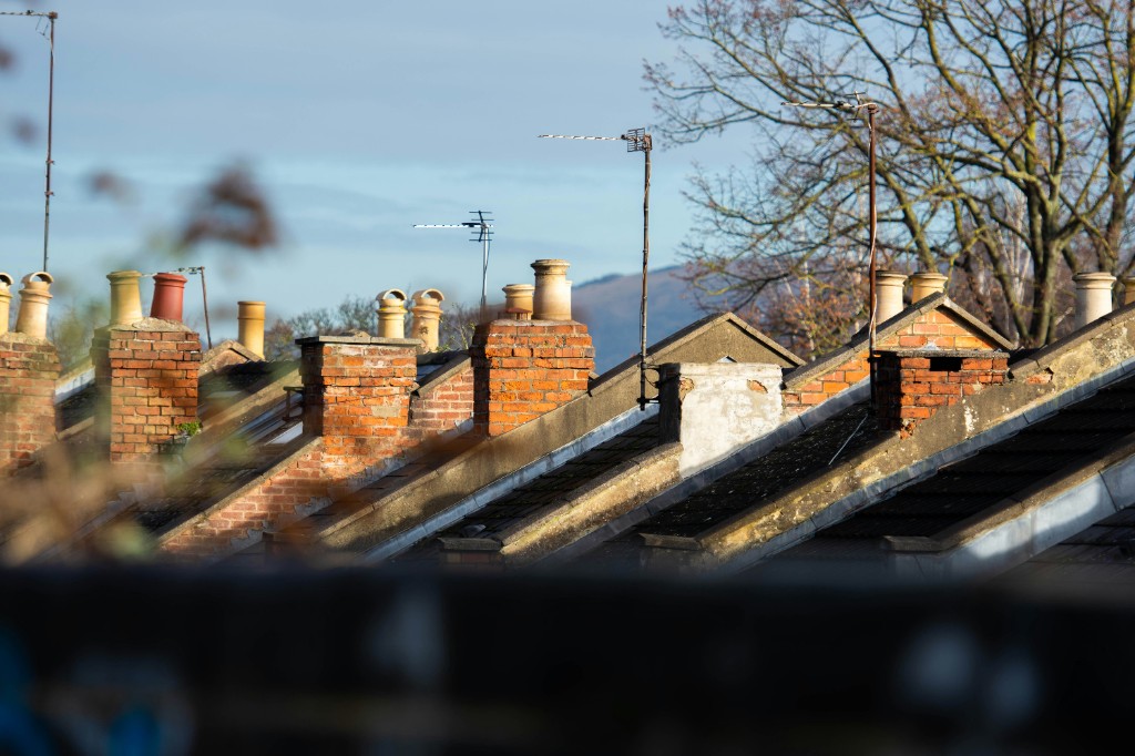 A row of brick chimneys and rooftops on terraced houses under a clear sky